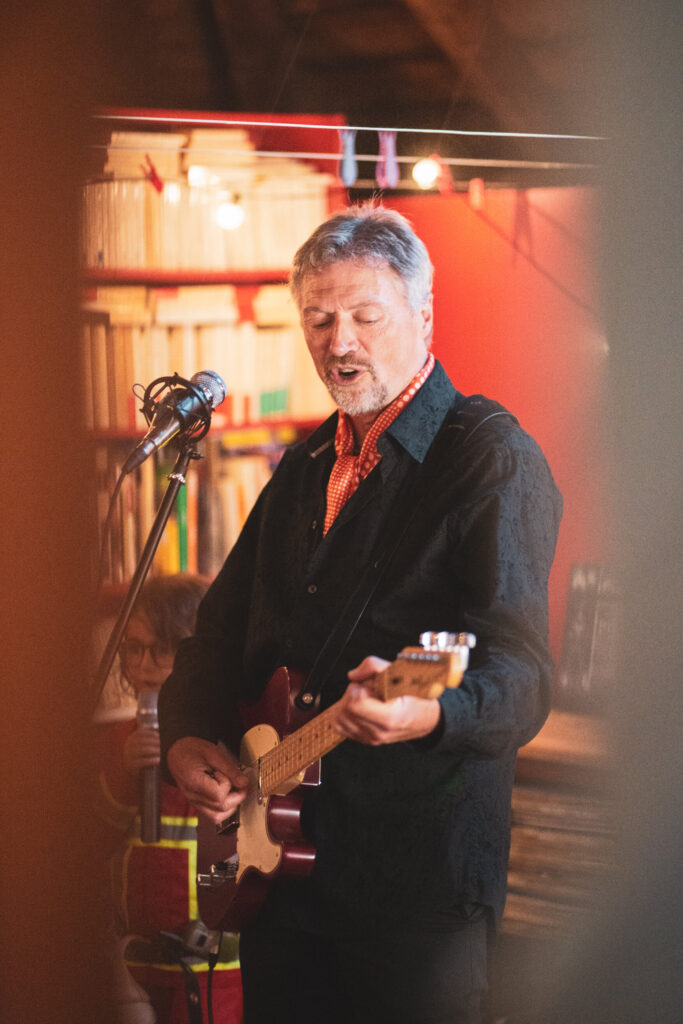 Michel jouant de la guitare électrique et chantant au micro lors d’un concert intimiste
